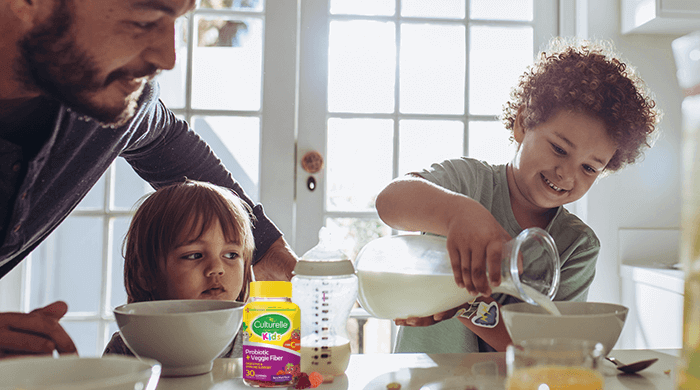 family at the table pouring milk into cereal bowl with Culturelle Kids gummies on the table
