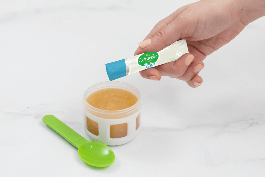 hand pouring baby healthy development packet into apple sauce